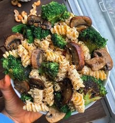 a white bowl filled with pasta and broccoli on top of a wooden table