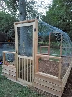 a wooden structure with a glass door on top of it in the grass next to a tree