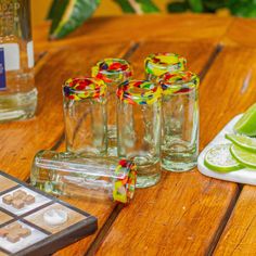 four shot glasses sitting on top of a wooden table next to sliced limes and marshmallows