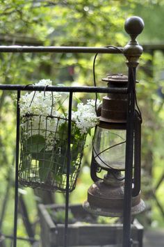 an old fashioned lantern with flowers in it on a balcony railing, surrounded by greenery