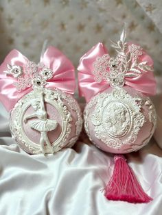 two pink ornaments with tassels and bows on them sitting on a white cloth