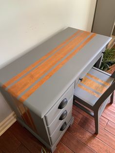 a grey desk with orange stripes painted on the top and bottom, next to a potted plant