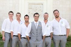 a group of men standing next to each other in front of a white building with flowers on their vests