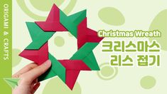 a hand holding up a folded origami christmas wreath with green and red stars