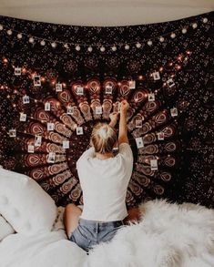 a woman sitting on top of a bed in front of a wall hanging with pictures