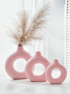 three pink vases sitting next to each other on a white counter top with dried grass in them