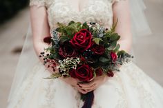 a bride holding a bouquet of red roses and greenery on her wedding day,