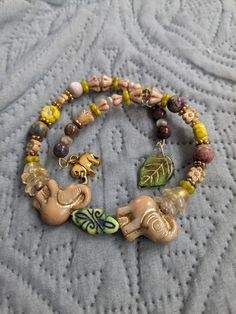 Lovely beaded charm Adjustable bracelet with two beige Chezh glass elephants and more! In the center of the elephants with raised trunks is a green Chezh glass bead with a painted black design. Chezh glass Flower beads in tan greens, and yellows. Goldstone spacer beads, and Round Jasper beads.  This is a double wrap bracelet and has two charms!  Gold tone elephant charm and a green Chezh glass leaf charm!  This bracelet is adjustable and will fit most wrists! Gift it for Mother's Day, Birthday, and more! Beaded Elephant, Elephant Charm Bracelet, Bead Flowers, Elephant Jewelry, Double Wrap Bracelet, Elephant Charm, Flower Beads, Leaf Charms, Jasper Beads