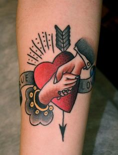 a tattoo on the arm of a person with a heart and arrow in it, holding hands