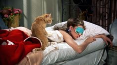 a woman laying in bed with a cat on her back and sleeping mask over her face