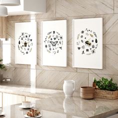 three framed pictures on the wall above a kitchen counter with plates and cups in front of them