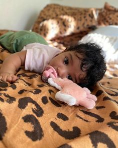 a small child laying on top of a bed with a stuffed animal in it's mouth