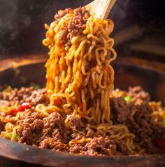 a wooden spoon full of noodles with meat and vegetables being lifted from the skillet