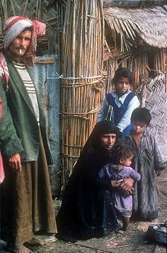 a group of people standing next to each other in front of a hut with thatched roof