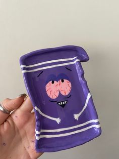 a hand holding up a purple cup with two faces painted on the outside and inside