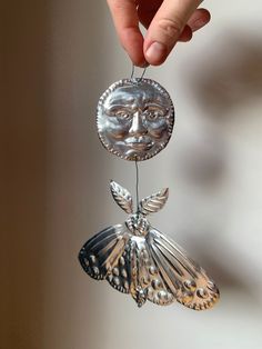 a hand holding a metal decoration with a face on it's head and wings