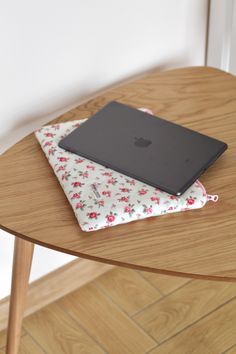 an apple laptop sitting on top of a wooden table next to a flowery cloth