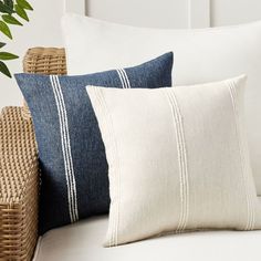 three pillows sitting on top of a white couch next to a wicker basket and potted plant