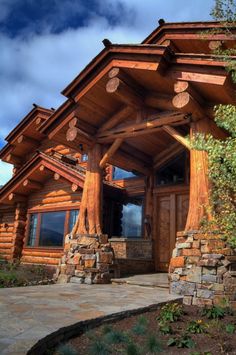 a large log home with stone pillars and wood trimmings on the front door