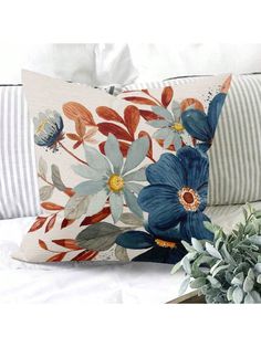 a blue flowered pillow sitting on top of a bed next to a potted plant