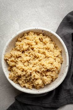 a white bowl filled with quinoa on top of a gray cloth next to a black napkin