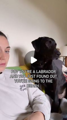 a woman sitting next to a black dog on top of a bed