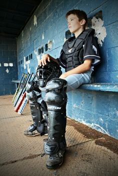 a young baseball player sitting on the bench with his catcher's gear in front of him