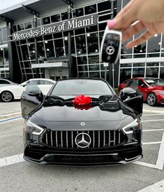 a person holding a car key in front of a black mercedes benz dealership with red bows on it