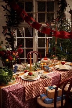 a table set for christmas dinner with candles, plates and presents on the dining room table