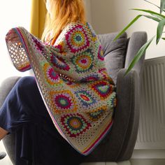 a woman sitting on a chair with a crocheted blanket