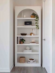 a white bookshelf with plants and other items on it in the corner of a room