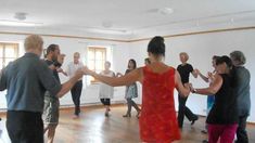 a group of people dancing in a room with wood flooring and large windows on the wall