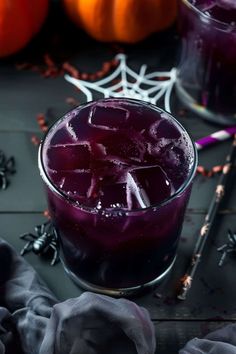 a glass filled with purple liquid next to two oranges and spooky spider web decorations