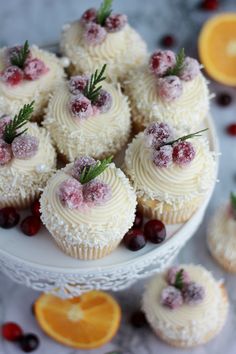 cupcakes with white frosting and cranberries on a plate next to orange slices