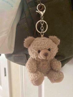 a brown teddy bear hanging from a metal hook on a door handle with a handbag in the background