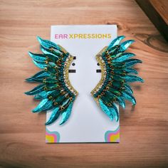 a pair of earrings with blue and green wings on top of a wooden table next to a book