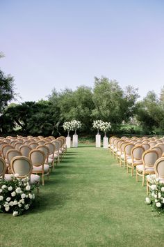 an outdoor ceremony with rows of chairs and white flowers on the aisle, in front of trees