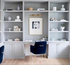 a living room filled with lots of white shelves and blue velvet chairs in front of it