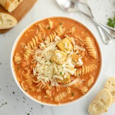 a bowl of pasta soup with bread and parmesan cheese