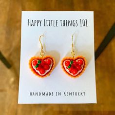 a pair of heart shaped earrings on top of a card with the words happy little things 101