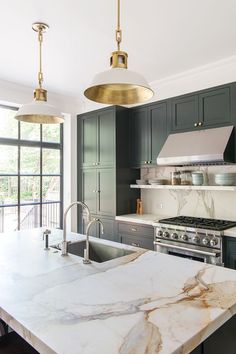 a large kitchen with marble counter tops and black cabinetry, along with two pendant lights hanging from the ceiling