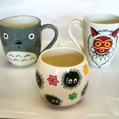 three mugs with different designs on them sitting next to each other, one has a cat face