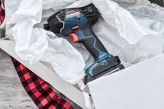 a cordless drill sitting in a box on top of a table next to some wrapping paper