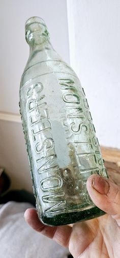 a person holding up a glass bottle with writing on it