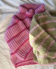 two knitted sweaters laying next to each other on a bed