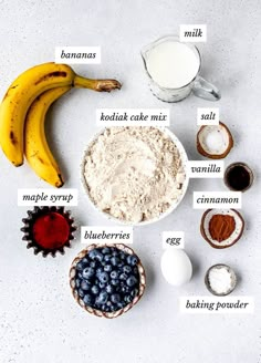 ingredients to make blueberry muffins laid out on a white surface with bananas