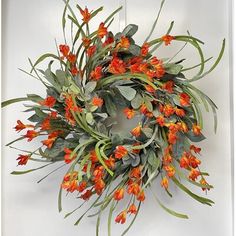 a wreath with orange flowers hanging on a door frame in front of a white wall