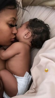 a mother kissing her baby while laying in bed