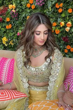 a beautiful woman sitting on top of a couch next to pillows and pillows in front of flowers