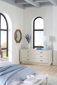 a white bedroom with arched windows and blue blankets on the bed, along with a large window